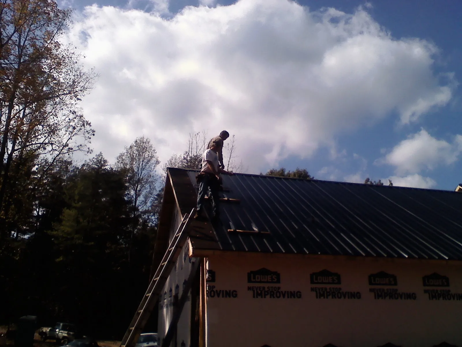 Roofer fastening dark metal panels high against a cloudy sky, from a Roof Inspection job in Daly City
